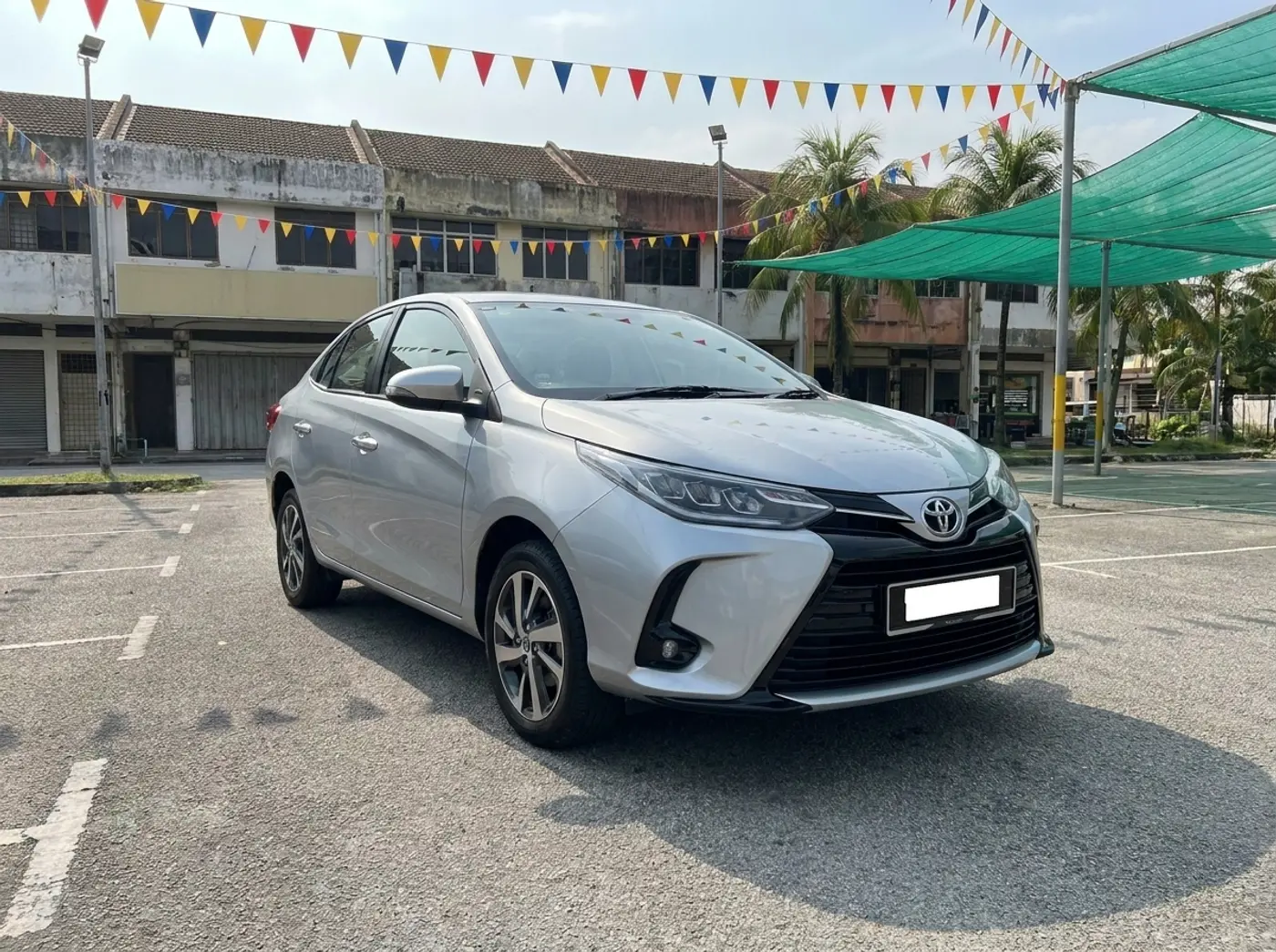 A silver Toyota Vios 1.5 G on the used-car lot under strings of bunting